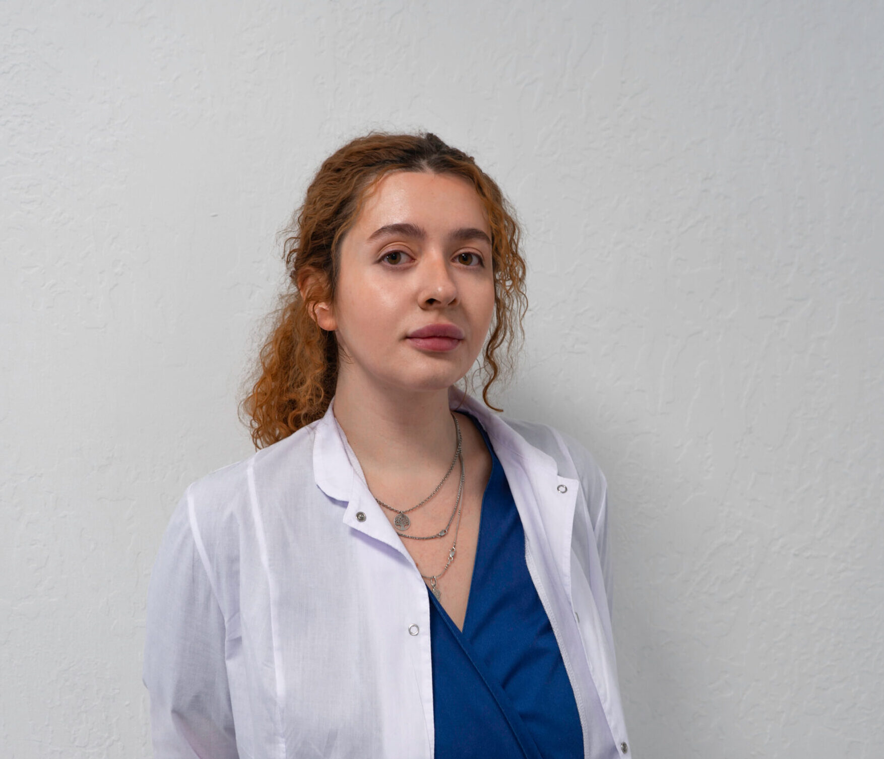 Лікар Олександра Литвинова у білому халаті на фоні світлої стіни. Вона хірург кисті
